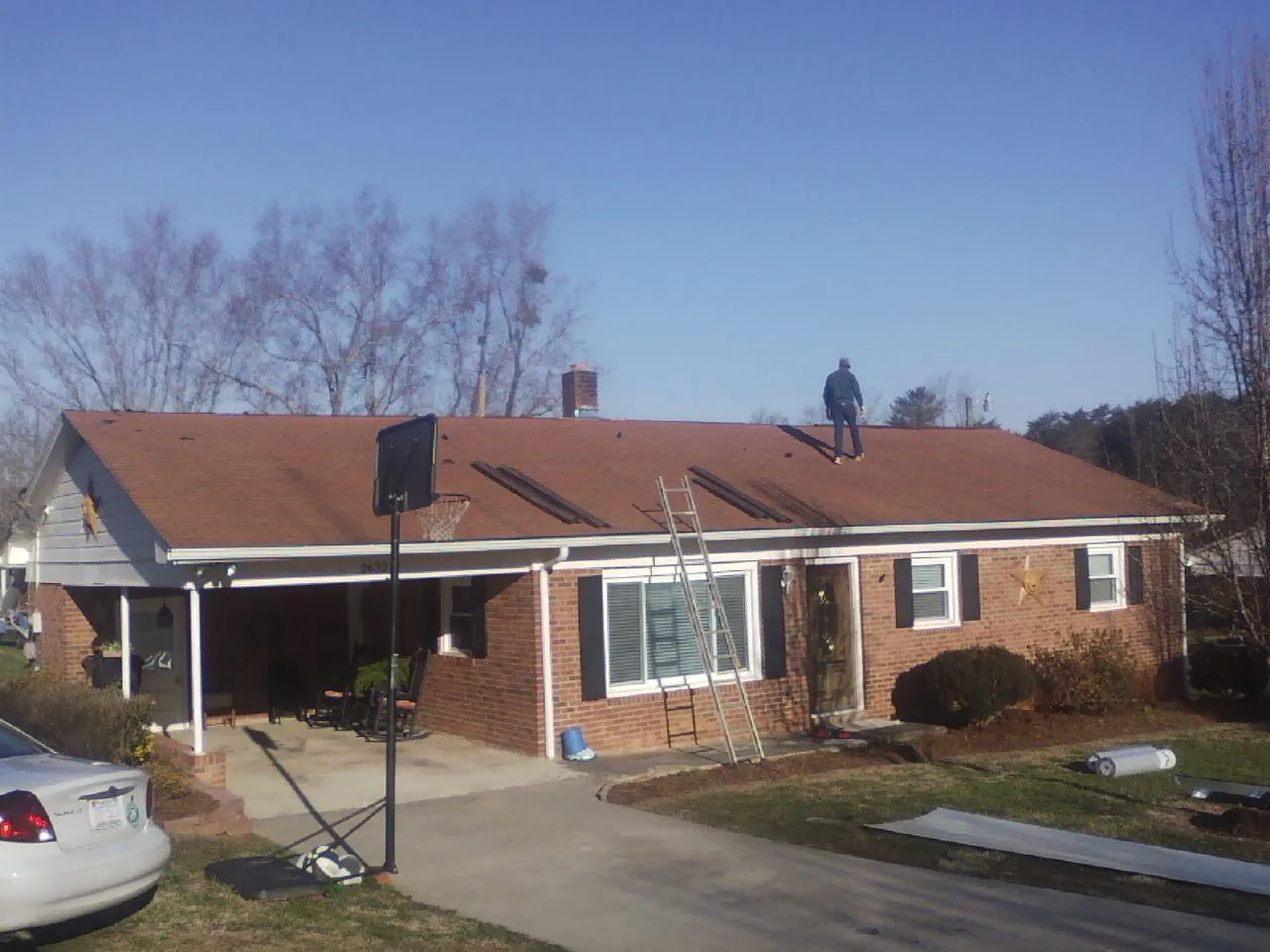 Roofer stripping a shingle roof on a brick ranch before metal panels in Wycombe