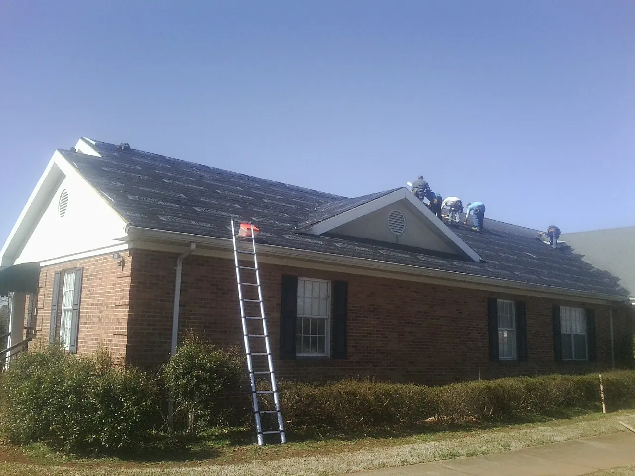 Crew tearing shingles off a brick ranch roof with a ladder set — Emergency Roof Repair work by our crew in Wycombe