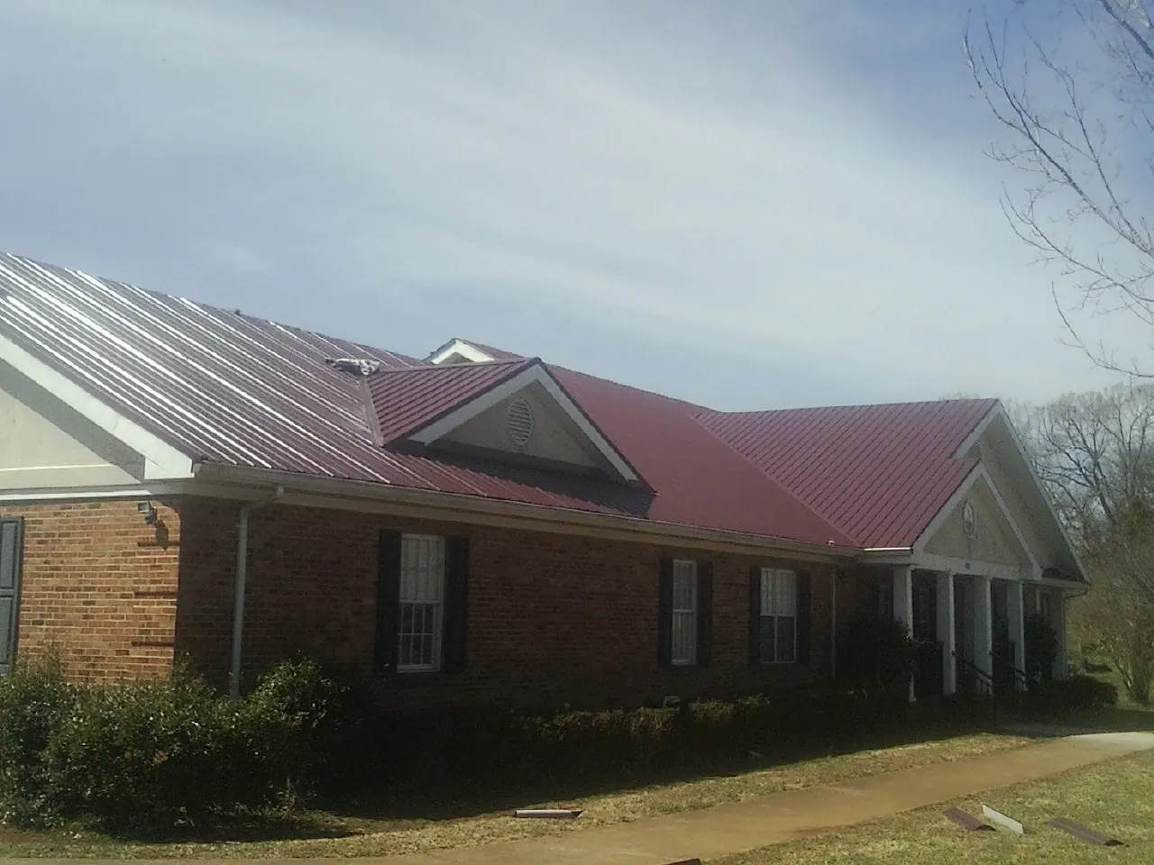 Red metal roof with gabled entries on a long brick building, from a Hail Damage Roof Repair job in Wycombe
