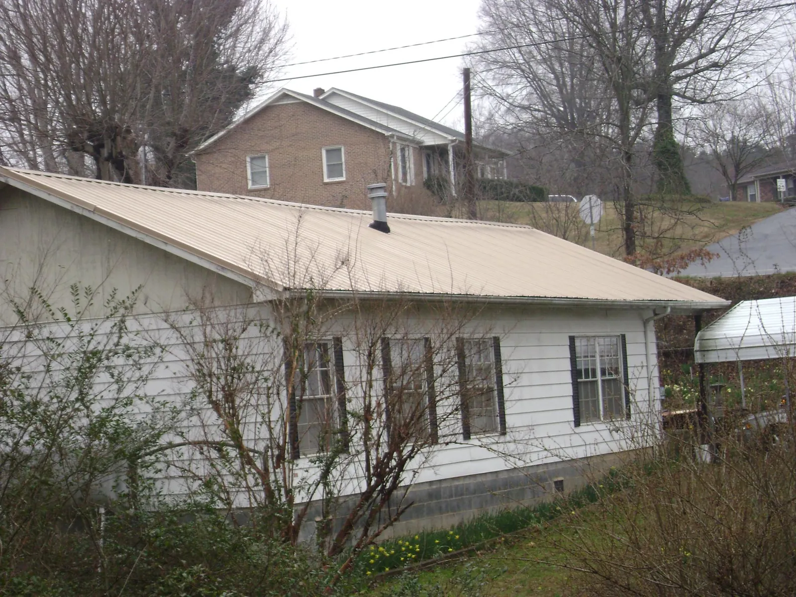 Tan metal roof on a white sided house set into a hillside — Commercial Roofing by Roofing Brothers in Wycombe